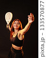 Woman poses confidently with a paddle racket in a dark studio setting 133570877