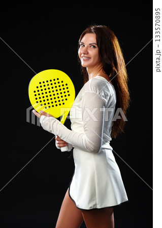 Young woman showcasing her skills with a bright yellow paddle in a sports studio 133570895