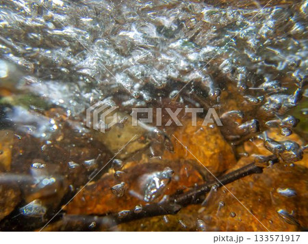 Abstract underwater image of colorful stream bubbles flow over stones twigs 133571917