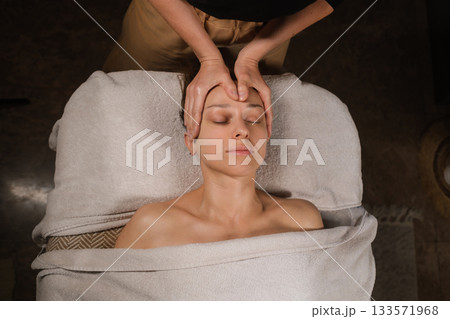 Relaxation therapy session showing a professional massage on a woman's head in a serene spa setting during the afternoon Relaxation therapy session showing a professional massage on a woman's head in a serene spa setting during the afternoon 133571968