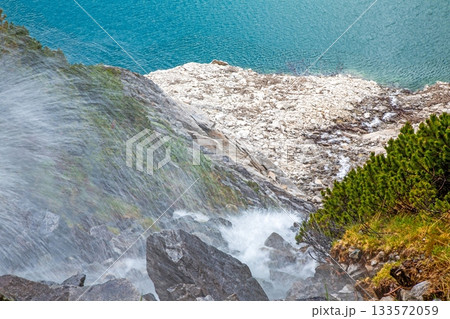 Steep mountain waterfall plunging toward turquoise alpine lake 133572059