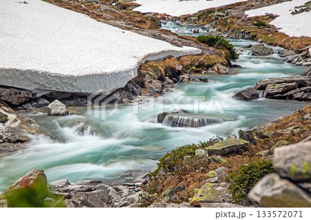 Turquoise alpine river cascading over rocks in snowy valley 133572071