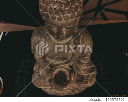 Stone Buddha statue in meditative pose, holding a bowl. Spiritual home decor accent with calm moody atmosphere, dim light and artistic texture. Perfect for mindfulness, zen, and meditation concepts. Stone Buddha statue in meditative pose, holding a bowl. Spiritual home decor accent with calm moody atmosphere, dim light and artistic texture. Perfect for mindfulness, zen, and meditation concepts. 133572702