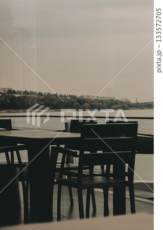 Outdoor dining area with a view of the lake on an overcast day. A table, chairs with a serene lake view visible through the glass railing 133572705