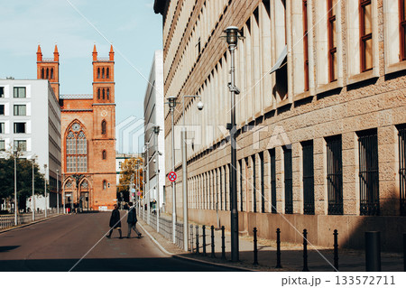 Berlin, Germany. 2 October 2022 Street scene with historic church and people walking across the road. A scenic view of historical architecture, including city dwellers crossing the road on a sunny day 133572711