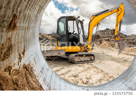 An excavator works at a construction site, moving dirt and earth under a cloudy sky, showcasing the machinery's power and activity on a busy day 133573750