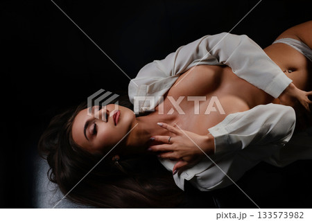 Beautiful woman in shirt laying against dark background, soft lighting Beautiful woman in shirt laying against dark background, soft lighting 133573982