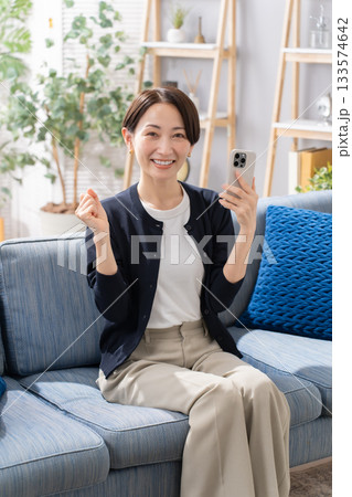 ソファーでスマホを操作する女性　ガッツポーズ 133574642