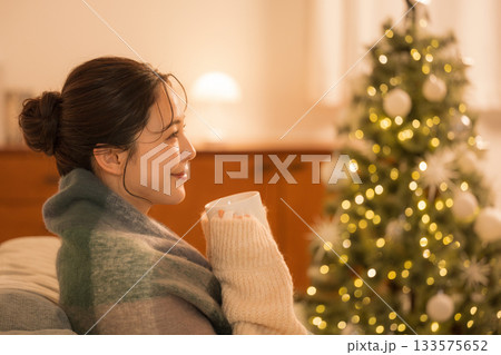 部屋でホットドリンクを飲む若い女性 クリスマスツリーと女性の冬イメージ 部屋でホットドリンクを飲む若い女性 クリスマスツリーと女性の冬イメージ 133575652