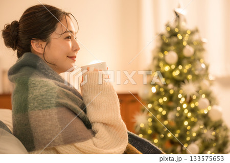 部屋でホットドリンクを飲む若い女性　クリスマスツリーと女性の冬イメージ 133575653