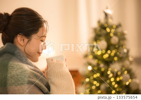 夜の部屋でホットドリンクを飲む若い女性 クリスマスツリーと女性の冬イメージ 夜の部屋でホットドリンクを飲む若い女性 クリスマスツリーと女性の冬イメージ 133575654