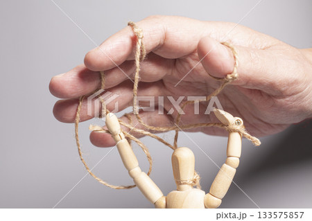 Man's hand pulling strings of wooden puppet on gray background. Concept of emotional manipulation,dictatorship and control 133575857