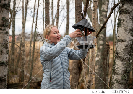 Woman refilling bird feeder in autumn forest 133576767