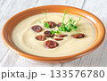 Creamy cauliflower soup with spicy chorizo served warmly in terracotta bowl on white table 133576780