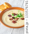 Terracotta bowl of creamy cauliflower soup paired with toasted baguette on bright wooden surface 133576781