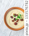 Creamy cauliflower soup with spicy chorizo served warmly in terracotta bowl on white table 133576782