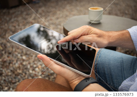 Person engages with a tablet while seated in nature Person engages with a tablet while seated in nature 133576973