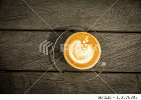 Latte art displayed in a glass cup on a wooden surface Latte art displayed in a glass cup on a wooden surface 133576985