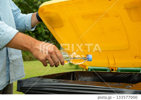 Person recycling a water bottle in a yellow trash bin 133577000