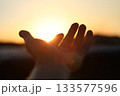 A hand reaching out toward the brightly rising sun, a New Year's sunrise background filled with hope for a brighter tomorrow and hopes and aspirations. 133577596