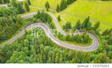 Winding asphalt roads snake through the green Alps, creating breathtaking views for travelers on an adventurous road trip, perfect for drone enthusiasts looking for stunning aerial perspectives. 133578201