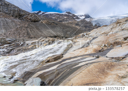 Water cascades down the rocky landscape near Schlaten Glacier, showcasing the stunning contrast of the rushing stream against the rugged terrain. This glacial area reflects beauty of Austrian Alps 133578257