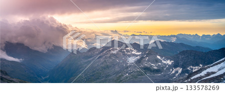 Rocky alpine mountains morning panorama. Cloudy sunrise on summer day. Grossglockner Mountain, Hohe Tauern National Park, Austrian Alps Rocky alpine mountains morning panorama. Cloudy sunrise on summer day. Grossglockner Mountain, Hohe Tauern National Park, Austrian Alps 133578269