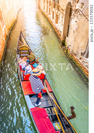 Visitors glide through the tranquil canals of Venice, Italy, enjoying a scenic gondola ride. The historic buildings and serene waters create a mesmerizing experience under the sun. Visitors glide through the tranquil canals of Venice, Italy, enjoying a scenic gondola ride. The historic buildings and serene waters create a mesmerizing experience under the sun. 133579092