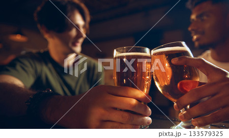 Closeup of beer glasses in hands during friendly toast at pub counter Closeup of beer glasses in hands during friendly toast at pub counter 133579325