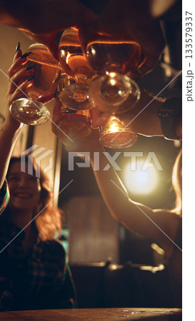 Beer glasses raised together in warm pub lighting scene Beer glasses raised together in warm pub lighting scene 133579337
