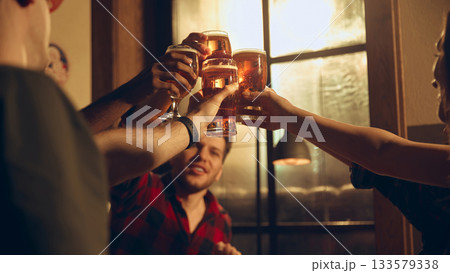 Friends cheering beer glasses in evening pub atmosphere 133579338