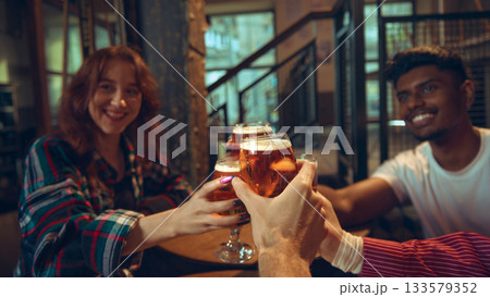Group raising beer glasses around pub table in warm interior Group raising beer glasses around pub table in warm interior 133579352