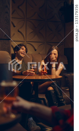 Couple laughing with beer mugs in intimate pub corner Couple laughing with beer mugs in intimate pub corner 133579356