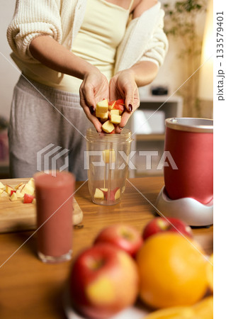 Hands placing chopped apples into blender cup while preparing fresh smoothie 133579401