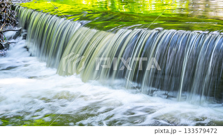 Small waterfall on the forest stream. Garden stone sluice in tranquil forest mood. 133579472