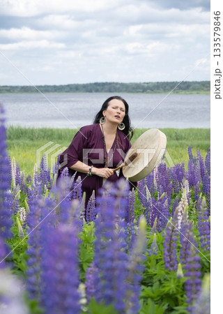 Shaman woman drumming among blooming flowers 133579846