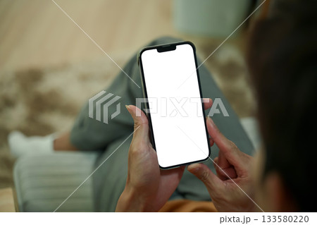 Close up of man hands holding a smartphone with white screen sitting on armchair 133580220
