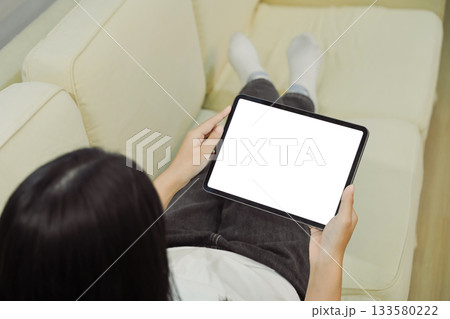 Close up view of a woman using blank screen digital tablet on sofa 133580222