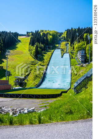Jested ski jumps in Liberec showcase the large ramps against a backdrop of lush green hills. A pleasant sunny day highlights the pristine condition of the ski area, ideal for winter sports. 133580426