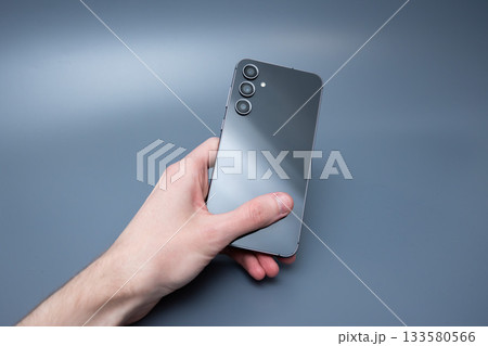 Modern smartphone with triple camera in hand on blue background for advertising 133580566