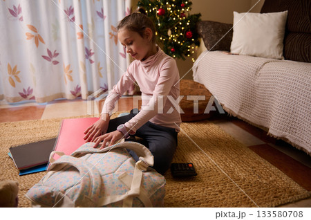 Young Girl Packing Backpack by Christmas Tree During Cozy Indoor Evening 133580708
