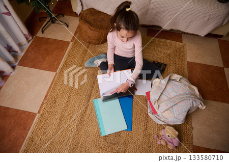 Young Girl Studying At Home With Notebooks, Backpack, And Cozy Rug 133580710