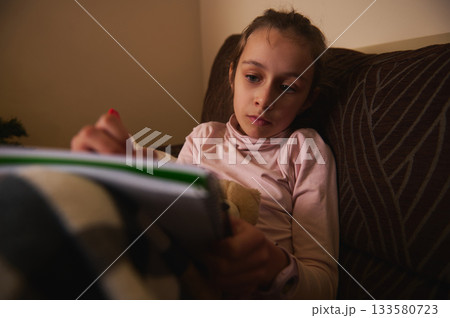 Girl Reading Book on Couch at Night Creates Cozy Home Moment 133580723
