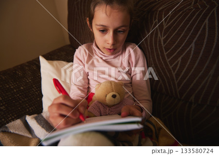 Young Girl Writing in Notebook with Teddy Bear on Couch, Cozy Home Scene 133580724