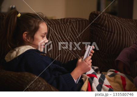 Young Girl Relaxing On Couch With Blanket, Looking at Cards In Cozy Home Setting Young Girl Relaxing On Couch With Blanket, Looking at Cards In Cozy Home Setting 133580746
