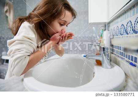 Young Girl Washing Hands At Bathroom Sink In Bright Tile Bathroom 133580771