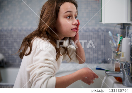 Girl Washing Face in Bathroom Sink During Morning Skincare Routine, Reflective Moment Girl Washing Face in Bathroom Sink During Morning Skincare Routine, Reflective Moment 133580794