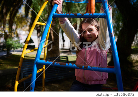 Young Girl On Colorful Playground Equipment Enjoying Outdoor Playtime In Bright Sunlight Young Girl On Colorful Playground Equipment Enjoying Outdoor Playtime In Bright Sunlight 133580872