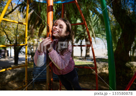 Joyful Girl Climbs Colorful Playground Structure on a Sunny Day at the Park 133580878