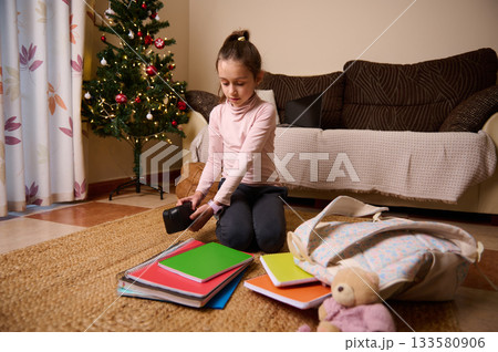 Young Girl Organizing School Supplies Near Christmas Tree At Home 133580906